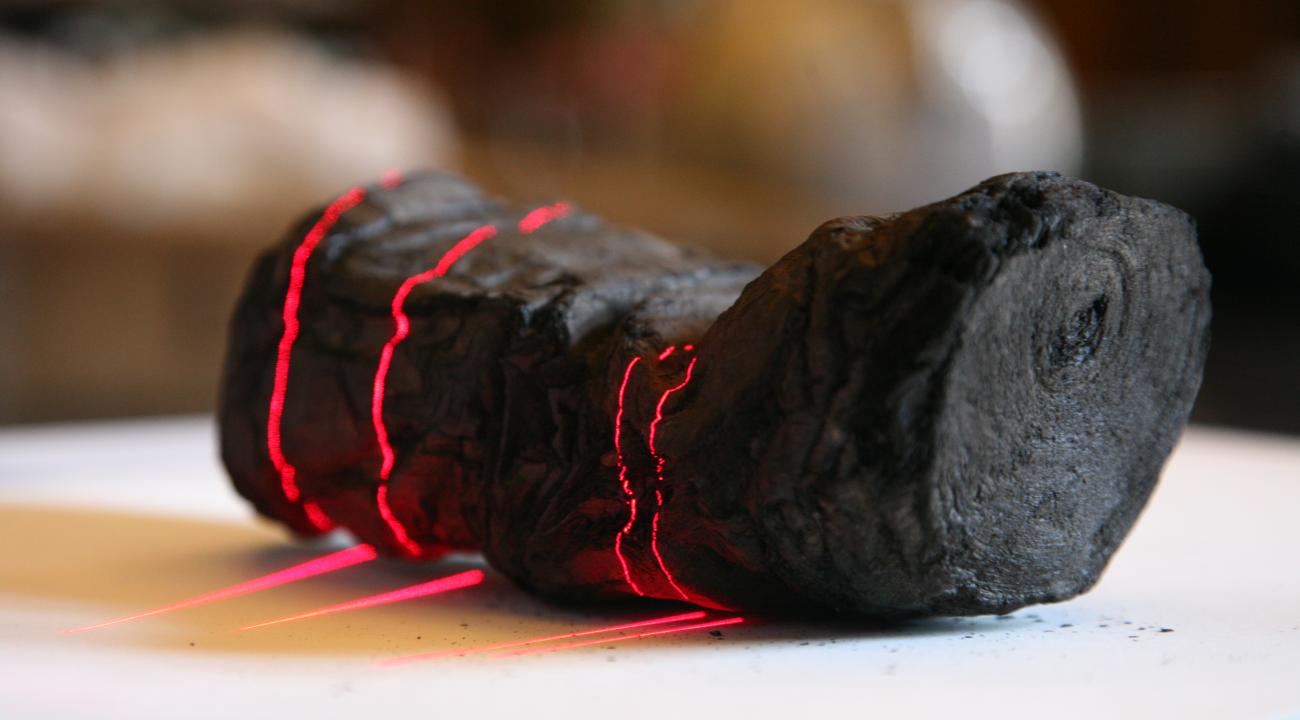 Carbonized Herculaneum scroll undergoing scanning, with red laser lines across its surface